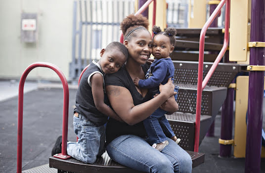 A woman smiling and hugging her kids on a playground.