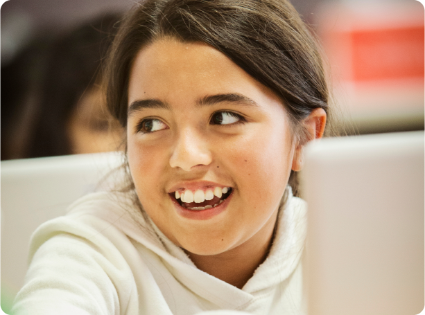 A student smiles and looks to the left while working on a computer in class.