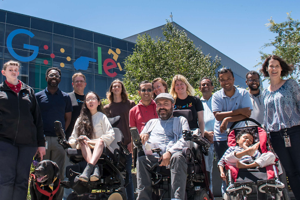 Members of Google’s Disability Alliance in front of a campus building featuring Google’s disability logo