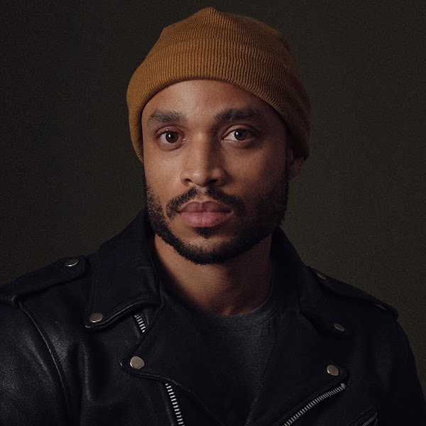 Portrait of artist in a brown beanie in front of a black background.