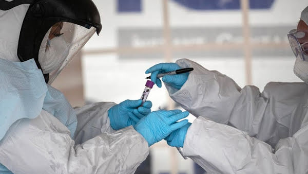 Two doctors in hazmat suits handling off a test tube in a lab.