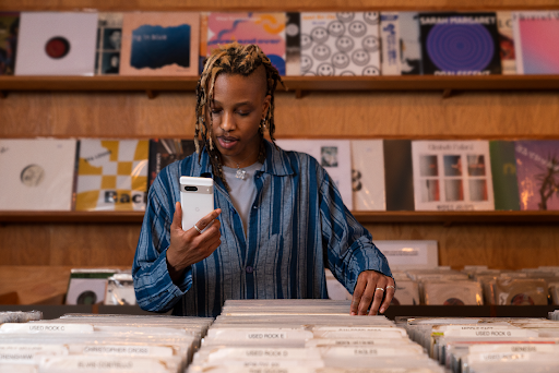 A shopper in a record store checks their Pixel 7 phone. They’re wearing a blue button down over a gray shirt.