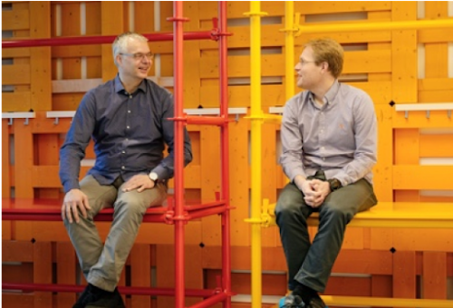 Two men talking, sitting on metal shelves.