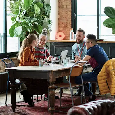 أربعة زملاء في العملاء مجتمعون حول طاولة اجتماعات في مكتب تحيط به النباتات
