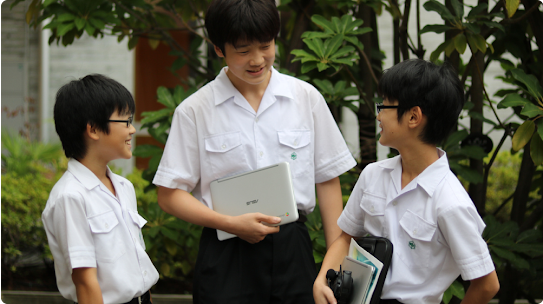 Three young male students wearing identical white collared shirts stand talking to each other and smiling.