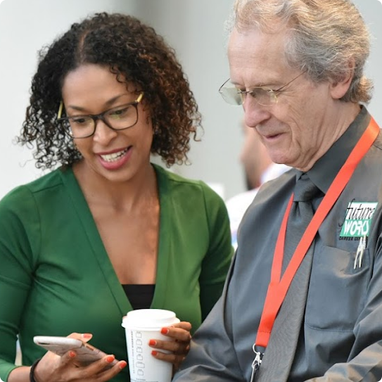 A woman shows a man something on her phone. The woman is smiling.