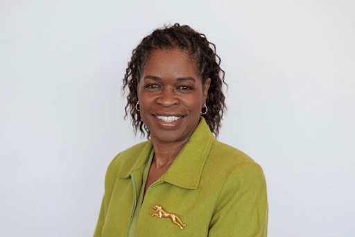 A Black woman wearing a green blazer smiles at the camera