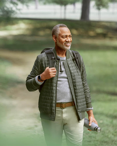 A senior male walking through a park wearing a Fitbit device