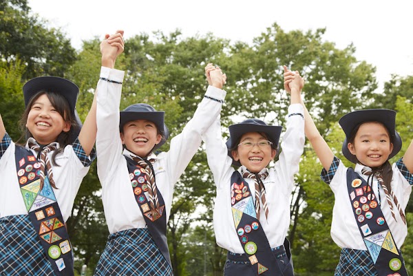 Four Japanese girl scouts stand together with their arms raised in celebration.