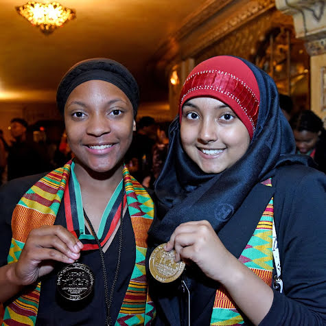 Two young women with colorful scarves holding up medals.