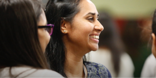 A woman with long straight hair is seen from her right side. She’s smiling while in conversation with other women.