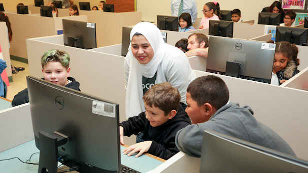 Profesora en un hiyab sonríe a dos jóvenes estudiantes varones en la computadora