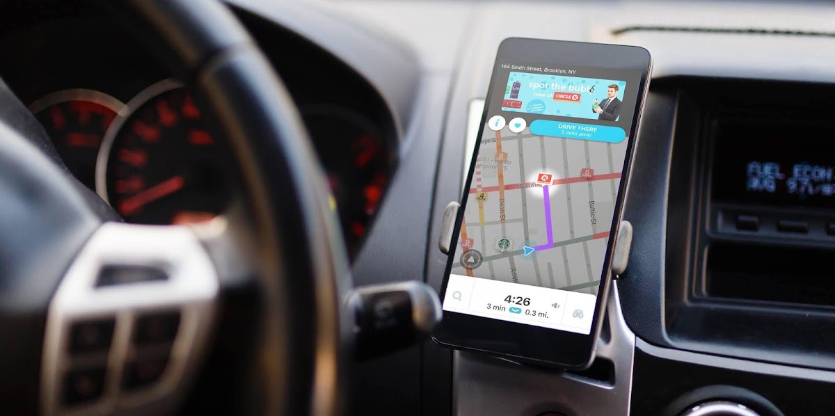A phone with a rests in a dashboard mount, Waze App directions show the driver as 1 left turn from its destination