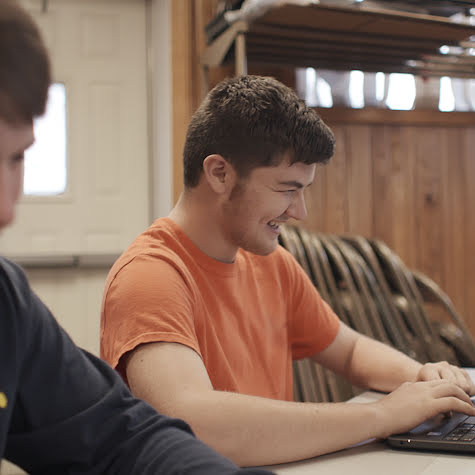 Two teenage boys working on computers and laughing.