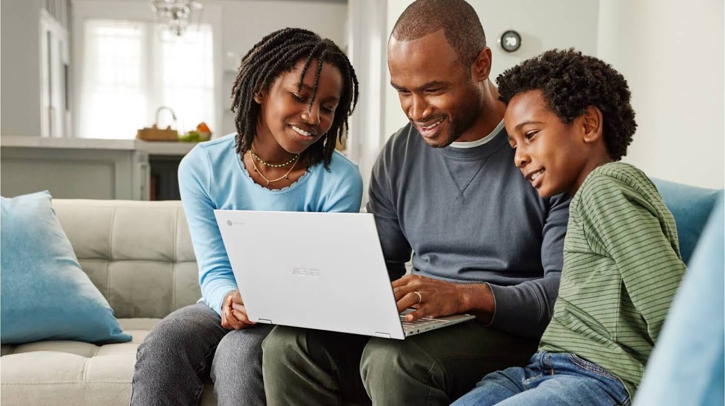 Un hombre trabaja con un Chromebook en casa acompañado por dos niños que observan su pantalla.