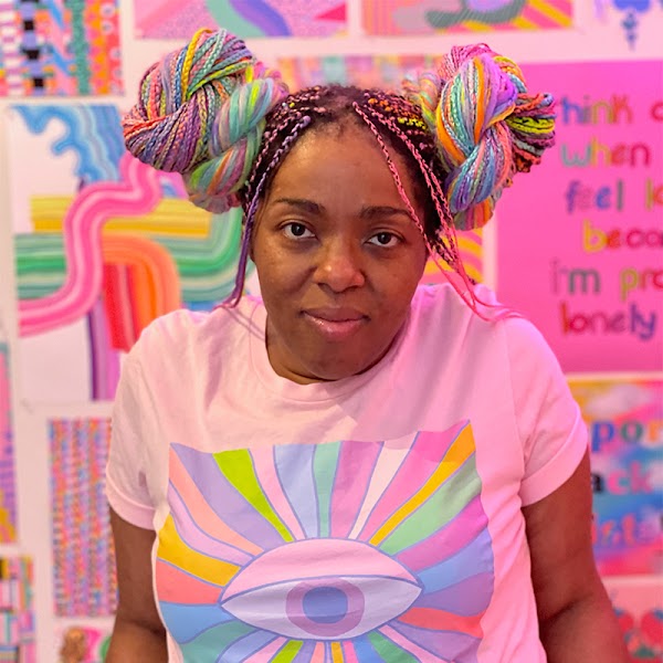 Portrait of artist with multi-colored individual braids in two buns wearing a pink shirt in front of their work.