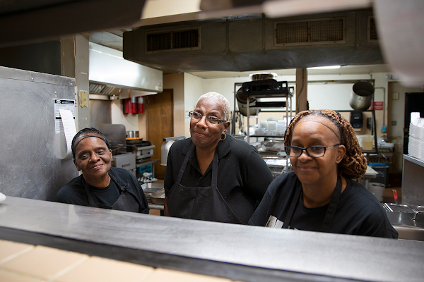 Three employees of the Four Way Restaurant stand behind a serving counter, ready to serve up smiles.