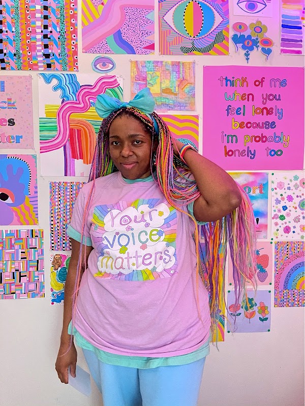 Artist with rainbow colored individual braids standing in front of their rainbow colored artwork.