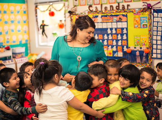 Una mujer sonríe mientras está en un aula rodeada de niños.