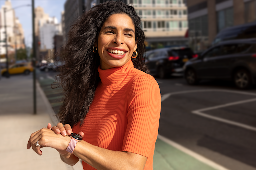 Een glimlachende smartwatchgebruiker staat op een stoep in het centrum van een stad en kijkt in de richting waar de Google Maps-app naartoe navigeert.
