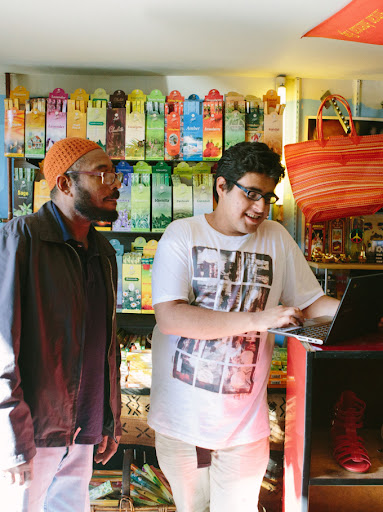 A young boy smiles and stands next to a shop-owner in a store while they look at a laptop together