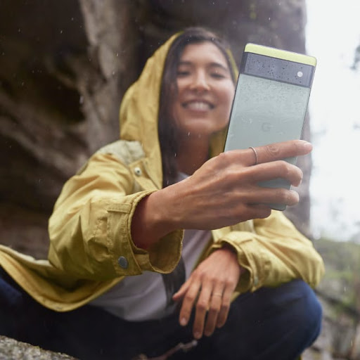 An adventurer on a mountain grins while they take a photo with their Pixel phone