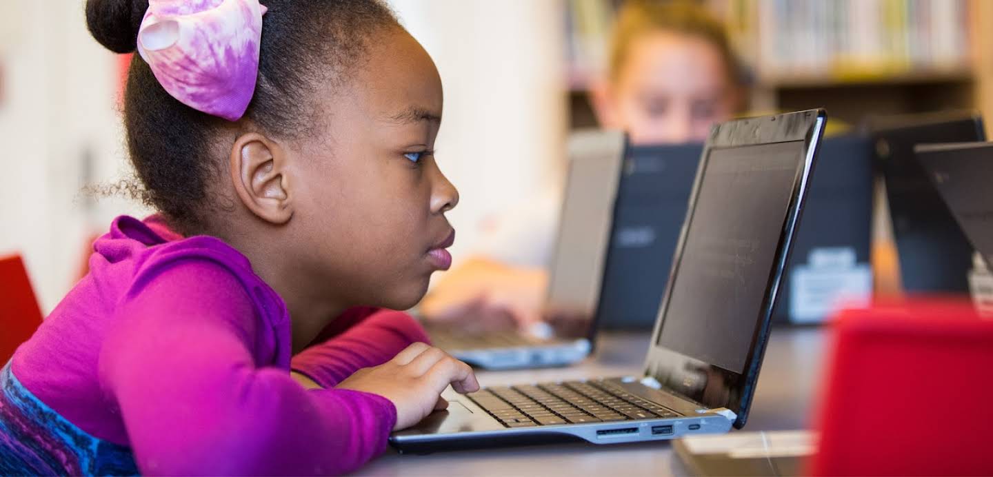 A young Black girl uses a Chromebook in a classroom.