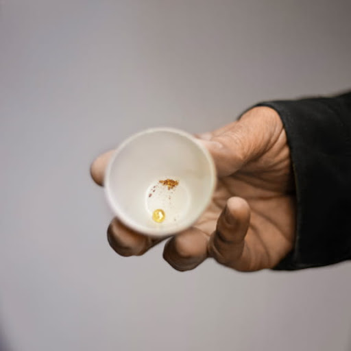 A hand holding a a small cup with gold ore at the bottom