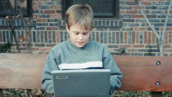 A blonde child sitting on a bench working on a laptop