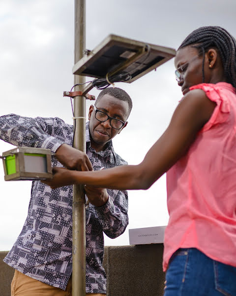 Engineer and a teammate installing a sensor on a rooftop in busy Kampala