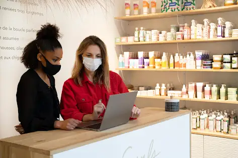 Deux femmes regardant un écran d’ordinateur dans une boutique de produit capillaire