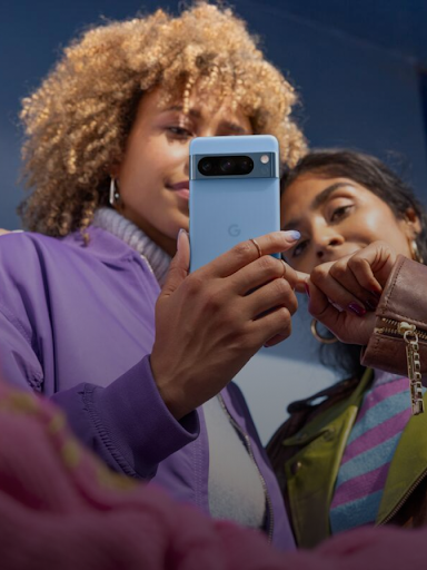 Zwei Android-Nutzerinnen schauen auf ein Smartphone.  Eine von ihnen zeigt auf eine Antwort auf dem Display.