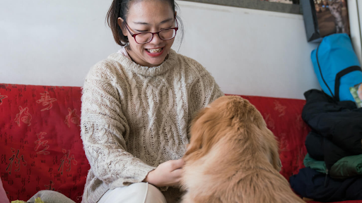 A woman sits on a red bench smiling while petting a dog in front of her