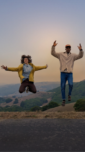 A couple of people are joyfully jumping in the air. The sky behind them has been altered to give it a golden hour hue using Magic Editor.