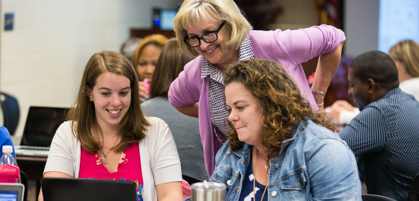 Tre kvinnor tittar på en laptopskärm under en konferens.