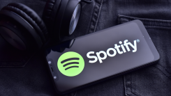 A smartphone with the Spotify logo rests on a pair of jeans next to a pair of headphones