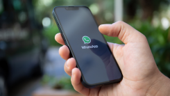A photograph of a man's hand holding a phone that's displaying the WhatsApp logo