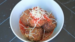 Fried meatballs in a bowl with tomato sauce and parmesan cheese.