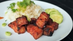 Chunks of pork belly on a plate with rice.