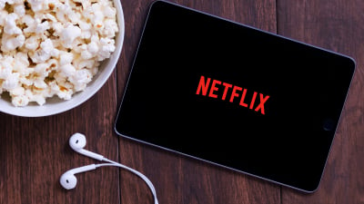 Netflix running on a tablet next to a pair of earbuds and a bowl of popcorn