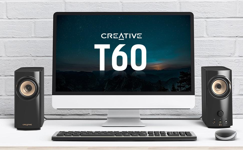 creative t60 desktop speakers on a tabletop setup beside a wide monitor