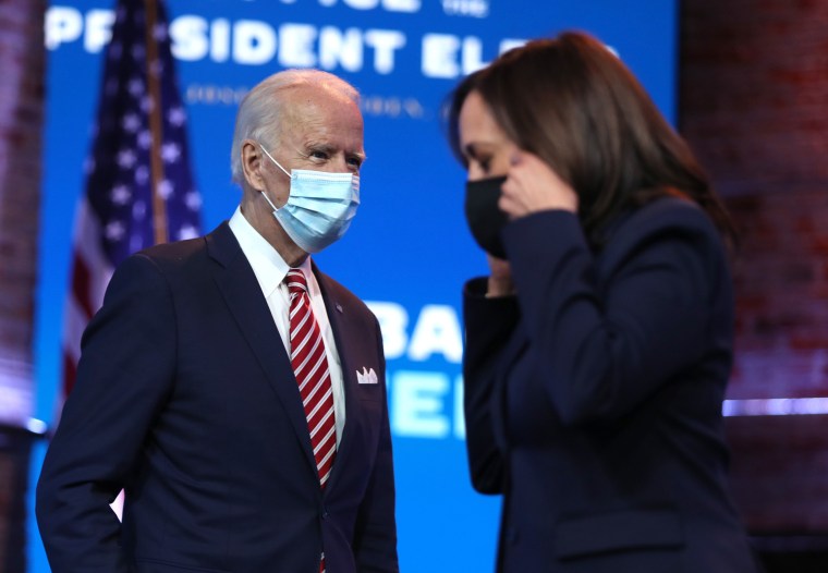 Image: President-elect Joe Biden walks by Vice President-elect Kamala Harris during a press briefing at the Queen Theater