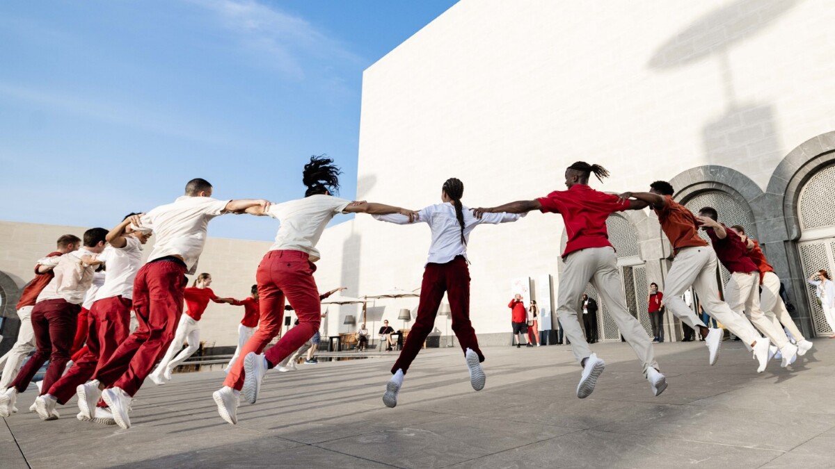 People wearing red and white dancing and jumping in a circle in front of a white building.