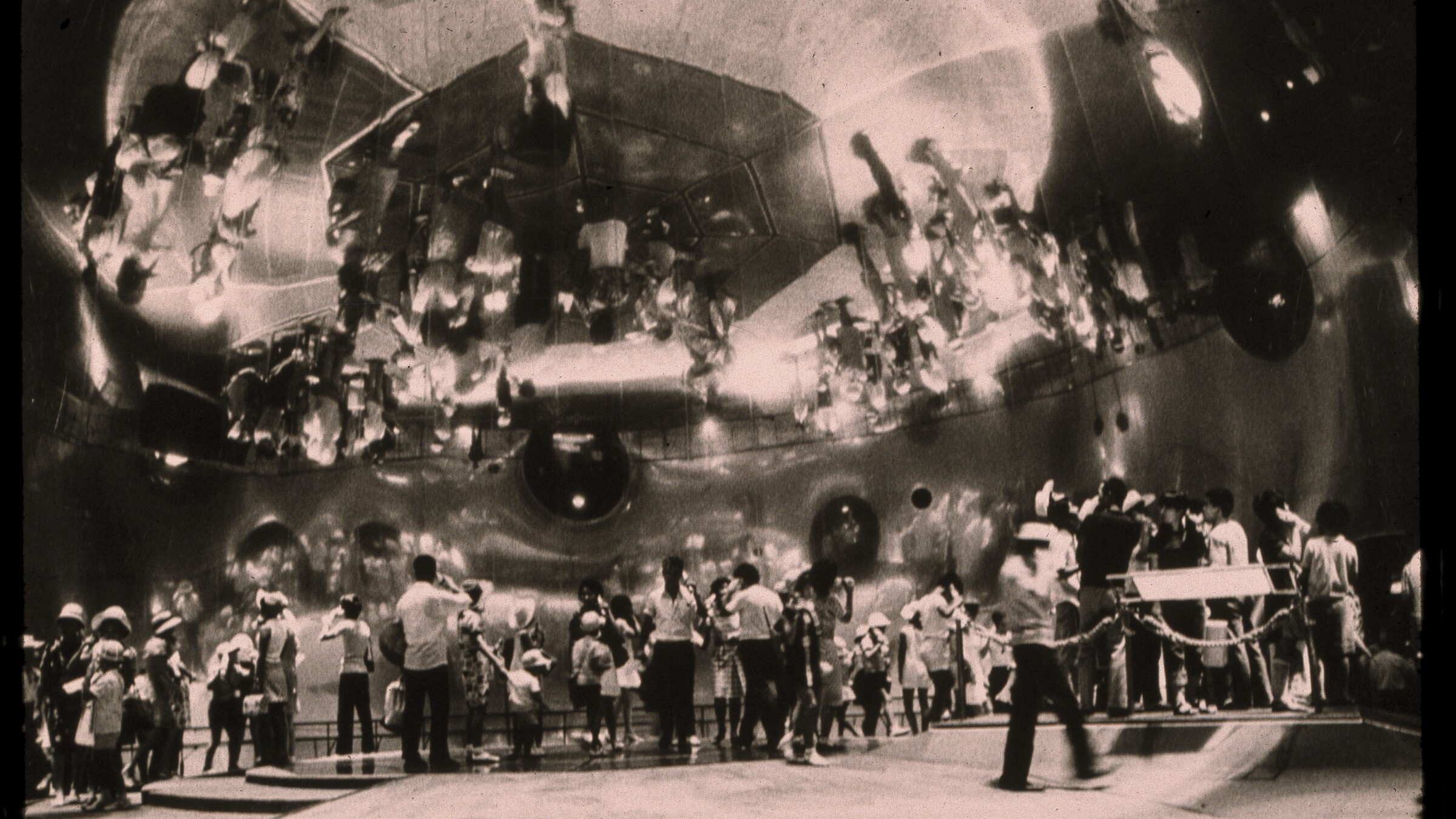 Black and white photograph of various figures standing below a mirrored dome featuring a spherical reflection