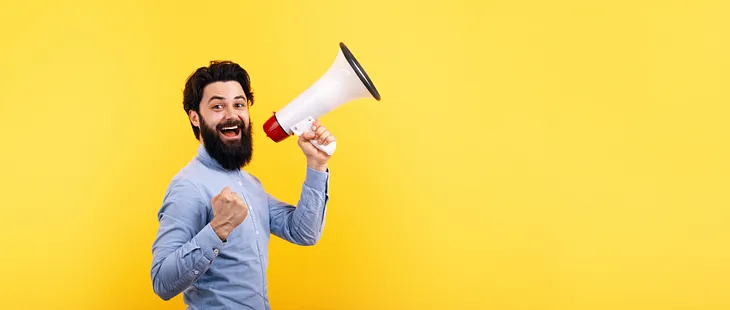 Male hipster man smiling and holding a megaphone over a yellow background,