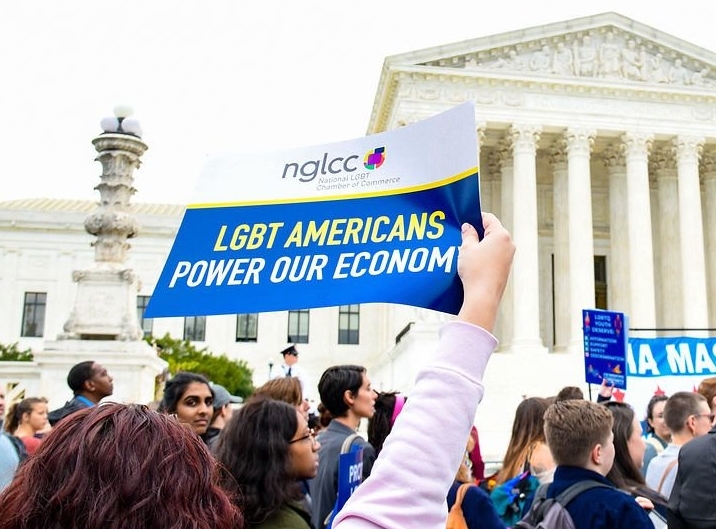 A woman holds up a sign reading "LGBT Americans Power Our Economy" alongside other protestors in front of the Supreme Court.