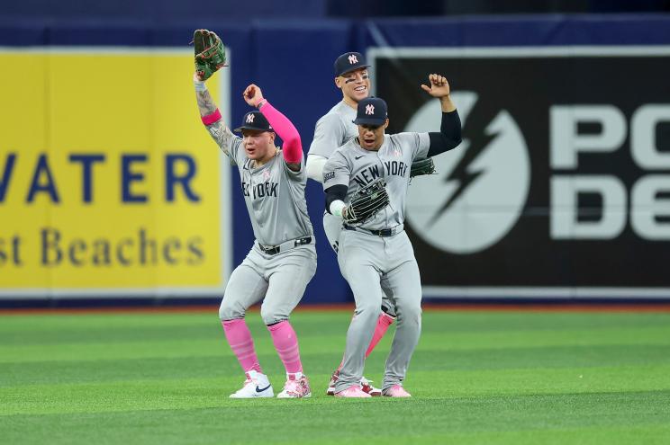 New York Yankees outfielders Alex Verdugo, Aaron Judge and Juan Soto celebrating a victory against the Tampa Bay Rays on a baseball field