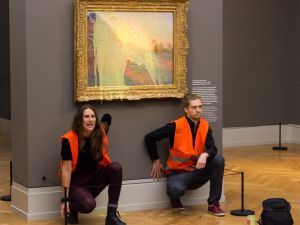 Two protestors kneel in front of a Monet with mashed potatos thrown on it.
