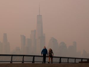 People in masks walk along the Hudson River as thick smoke shrouds the skyline of lower Manhattan.