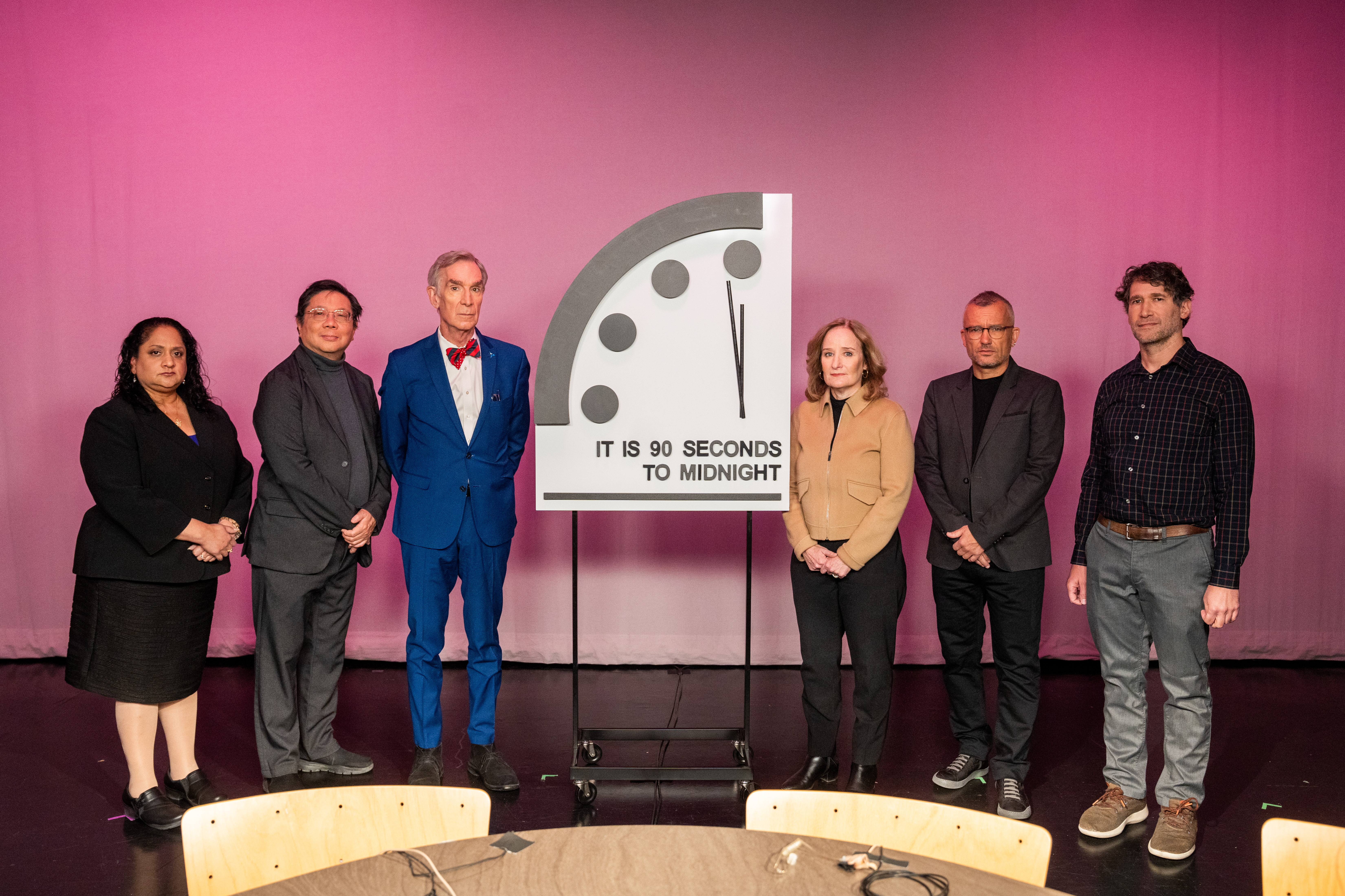 Group of people stand next to clock against pink background